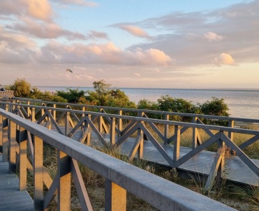 Drewniane przejście na plażę otoczone wydmami i niską roślinnością pokazuje naturalne otoczenie Jastarni. To charakterystyczna droga prowadząca turyst&oacute;w prosto nad zatokę.
